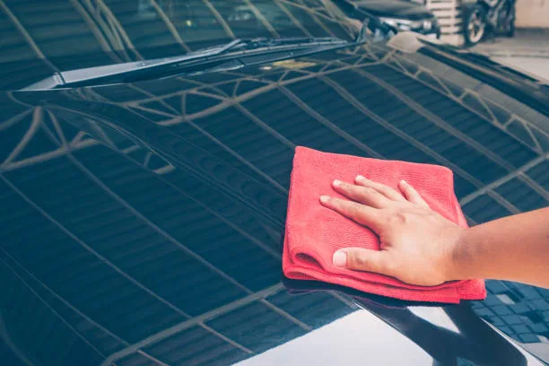 worker cleaning black car with microfiber red cloth.